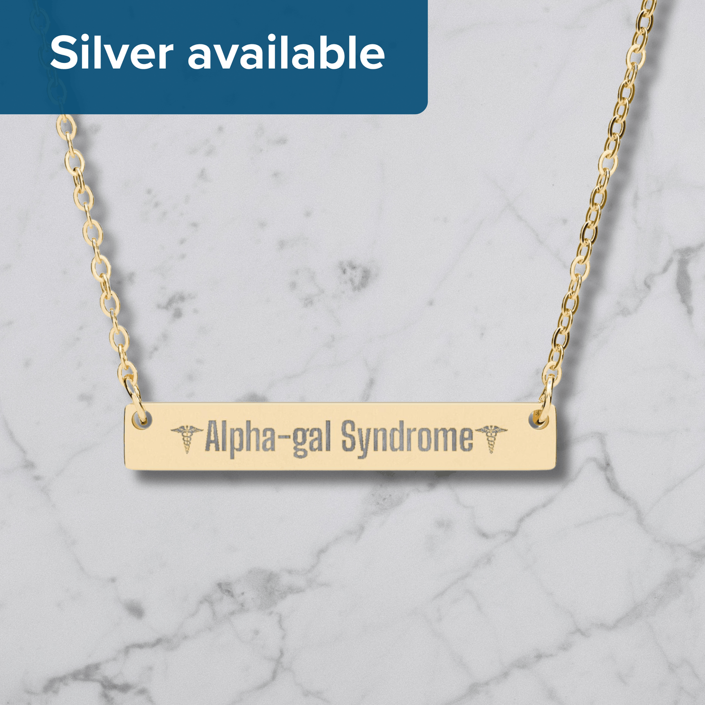 A gold bar necklace engraved with 'Alpha-gal Syndrome' and caduceus symbols, shown on a white marble background with a blue banner reading 'Silver available'.